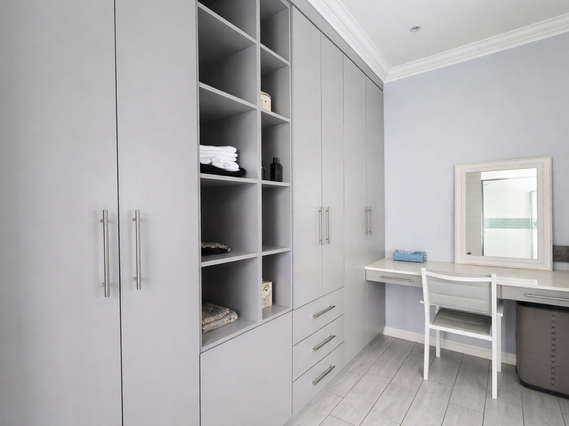 A well-appointed bedroom featuring extensive built-in cabinetry with integrated shelving and a dedicated vanity area, finished with modern tiled flooring and crown molding.