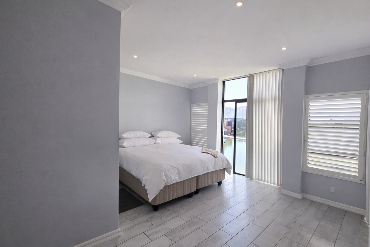 A bright, modern bedroom featuring tiled flooring, recessed lighting, and large glass doors with vertical blinds, offering natural light and views.