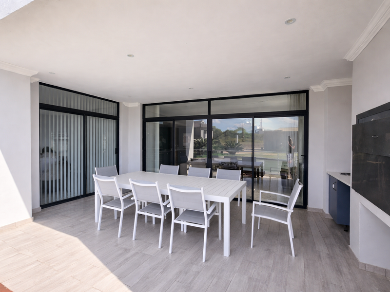 A spacious covered patio featuring tiled flooring, recessed lighting, a built-in braai, and large sliding glass doors providing seamless indoor-outdoor flow.