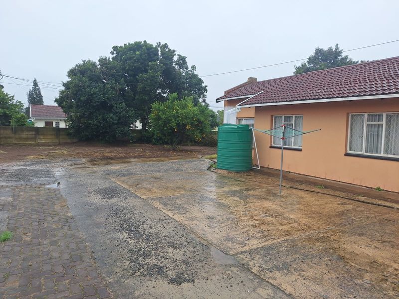 Rear exterior view of the property featuring a concrete driveway, water storage tank, and perimeter walling.