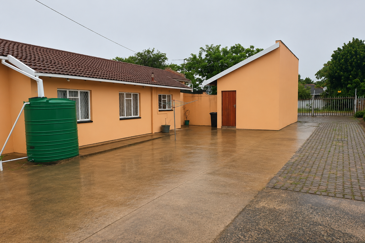 Rear exterior view of the property featuring a concrete paved courtyard, water tank, and access to a detached outbuilding.
