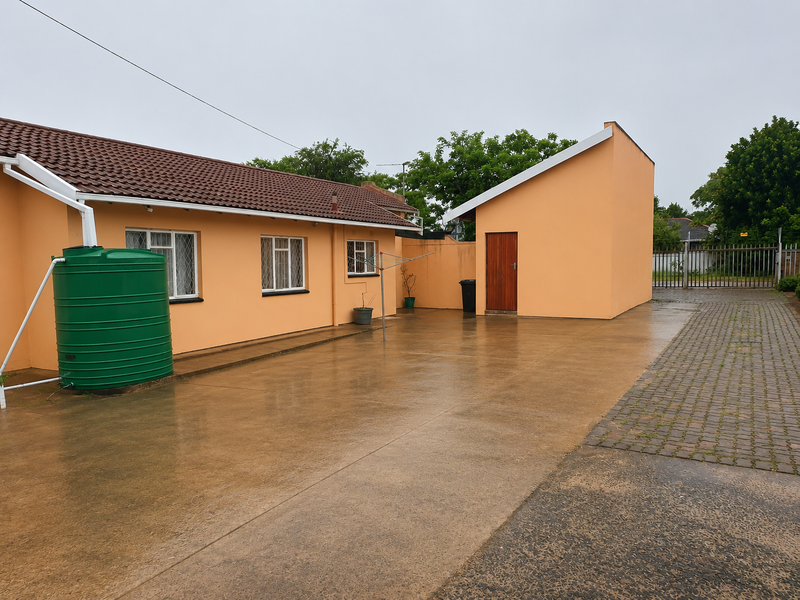 Rear exterior view of the property featuring a concrete paved courtyard, water tank, and access to a detached outbuilding.