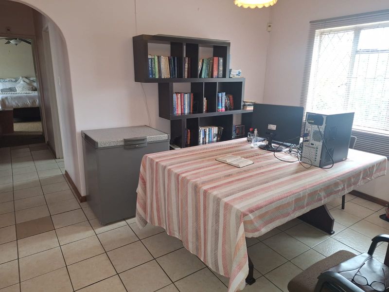 A functional home office space featuring ceramic floor tiles, an arched entryway, and a window fitted with security bars.