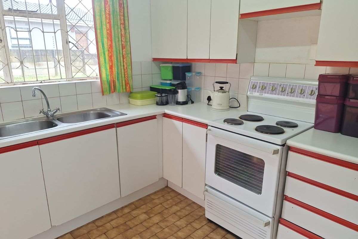 A functional kitchen featuring white cabinetry with red trim, a double basin sink, tiled backsplash, and a freestanding electric stove.