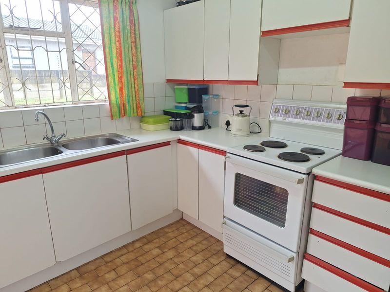 A functional kitchen featuring white cabinetry with red trim, a double basin sink, tiled backsplash, and a freestanding electric stove.