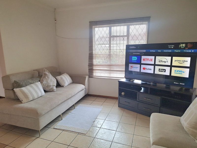 A functional living room featuring tiled flooring and a window fitted with venetian blinds and security bars.