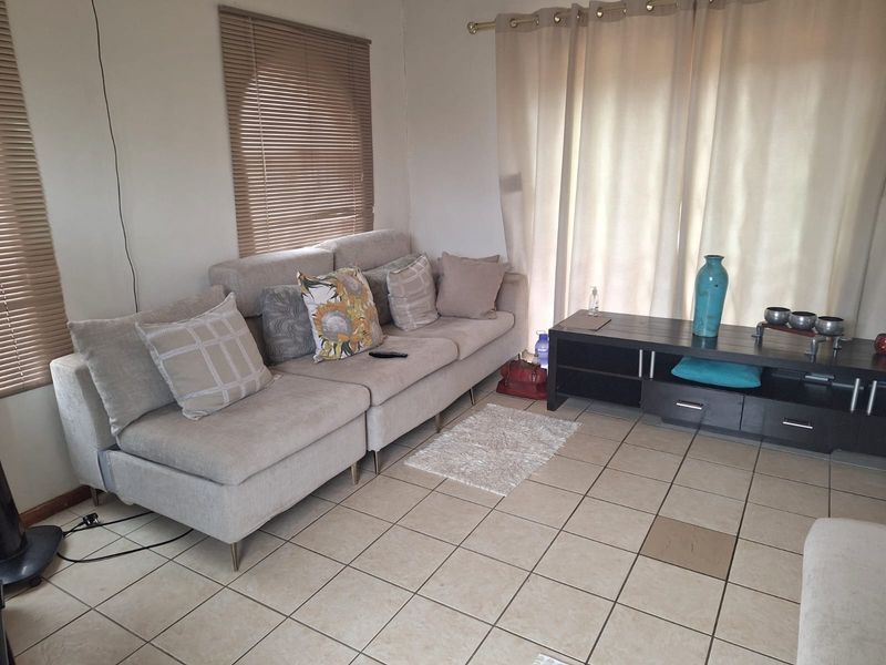 A living room featuring neutral tiled flooring and window treatments, providing a functional space with potential for cosmetic updates.