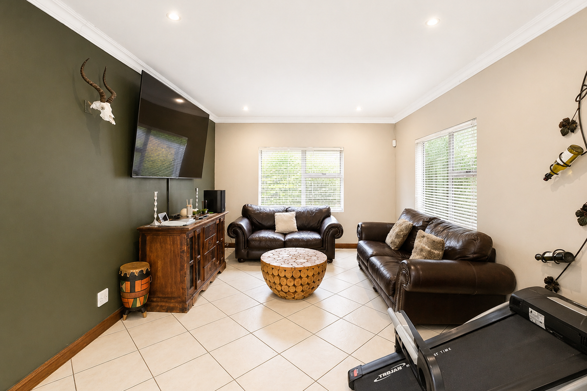 A well-maintained living room featuring tiled flooring, recessed downlighting, crown molding, and large windows with venetian blinds.