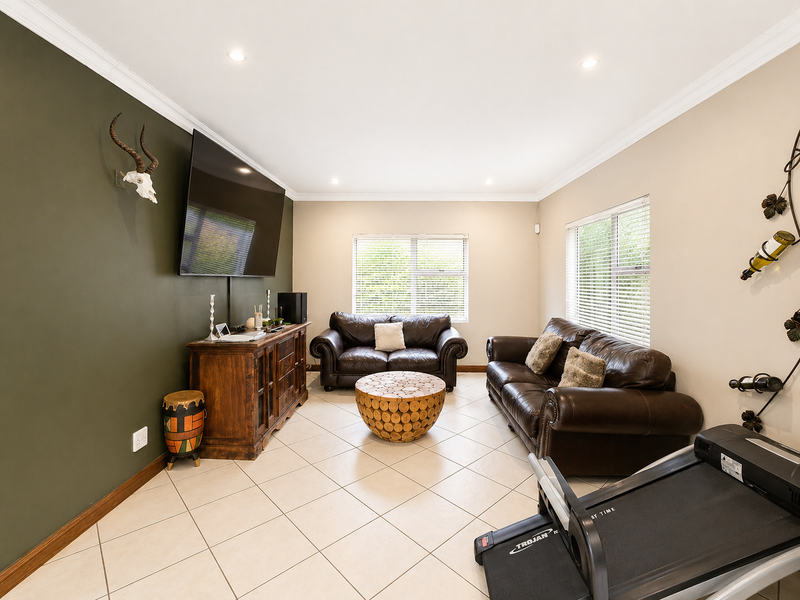 A well-maintained living room featuring tiled flooring, recessed downlighting, crown molding, and large windows with venetian blinds.