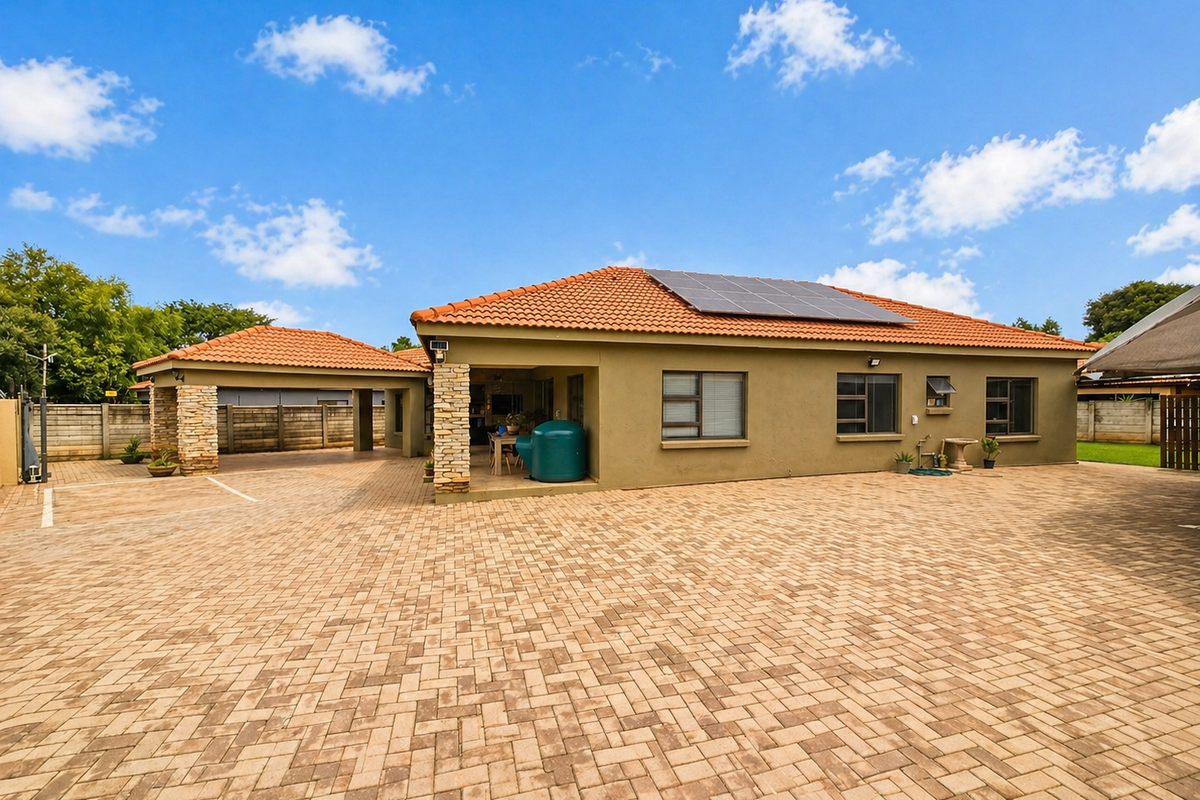 Spacious rear exterior view featuring a large paved driveway, covered patio area, stone-clad pillars, and roof-mounted solar panels.
