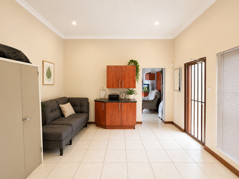 A bright living area featuring neutral tiled flooring, built-in cabinetry, recessed lighting, and a secure glass door leading to the exterior.