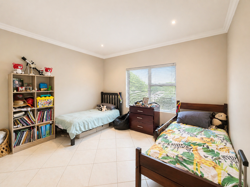A spacious bedroom featuring neutral tiled flooring, recessed downlighting, and large windows with venetian blinds, offering a clean and functional living space.