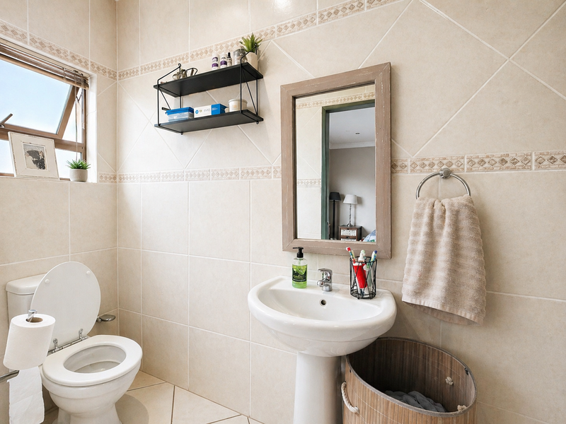 A well-maintained bathroom featuring neutral ceramic wall and floor tiles, a pedestal basin, and a top-hung window for natural ventilation.