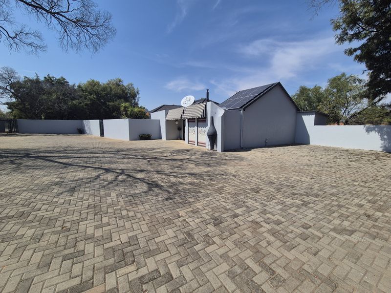 A wide-angle view of the property's front exterior, featuring a large paved driveway, perimeter wall, and solar panels installed on the roof.