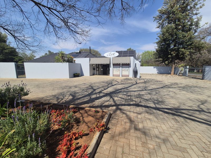 Front exterior view of the property featuring a large paved driveway, solar panels, and a covered entrance area with a built-in outdoor fireplace.