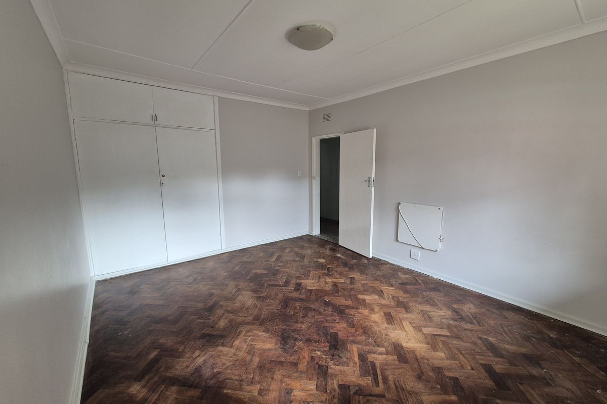 An empty bedroom featuring classic herringbone parquet flooring, built-in storage cupboards, and a wall-mounted heater.