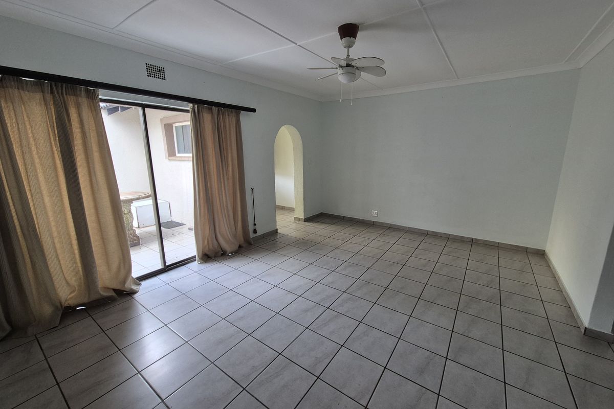Spacious, empty living room featuring neutral tiled flooring, a ceiling fan, and a sliding glass door providing access to the outdoor patio area.