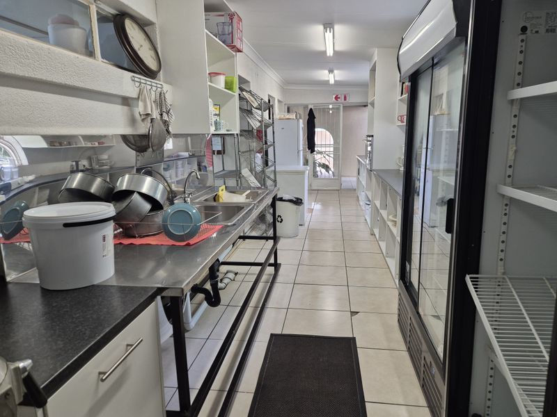 A functional scullery or prep area featuring stainless steel sink, commercial refrigeration, and ample built-in shelving with tiled flooring.