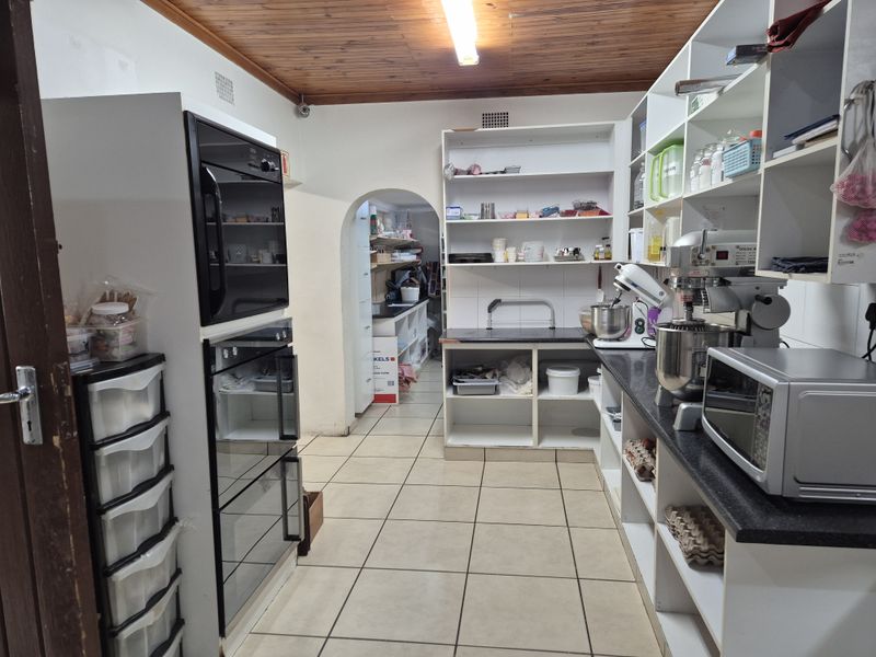 Functional scullery featuring built-in double ovens, extensive open shelving, stone countertops, and tiled flooring, with an archway leading to an adjacent space.