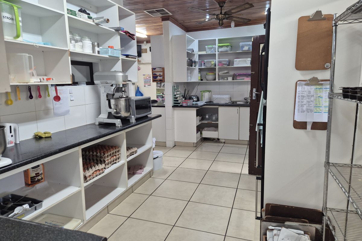 A functional kitchen featuring extensive open shelving, tiled flooring, and a timber-paneled ceiling, providing ample storage and workspace for food preparation.