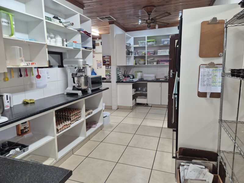 A functional kitchen featuring extensive open shelving, tiled flooring, and a timber-paneled ceiling, providing ample storage and workspace for food preparation.