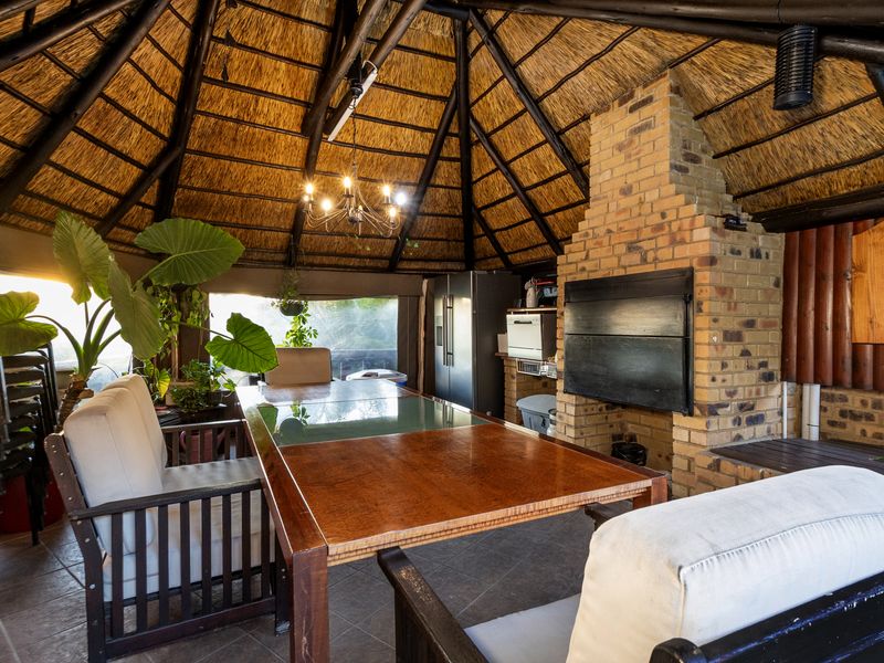 Covered outdoor entertainment area featuring a traditional thatched roof, exposed timber rafters, and a built-in brick fireplace, perfect for relaxed gatherings.