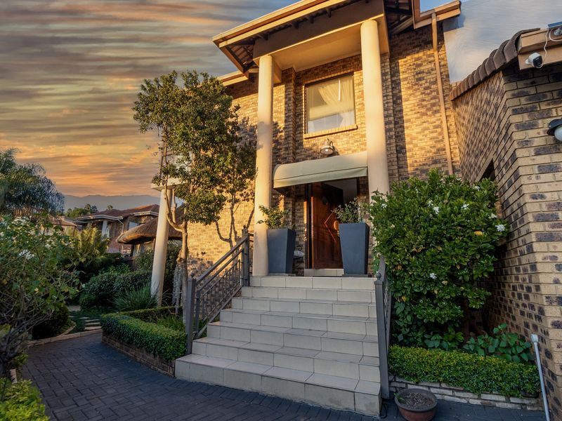 A well-maintained front entrance featuring a brick facade, tiled staircase with metal railings, and decorative columns under a sunset sky.