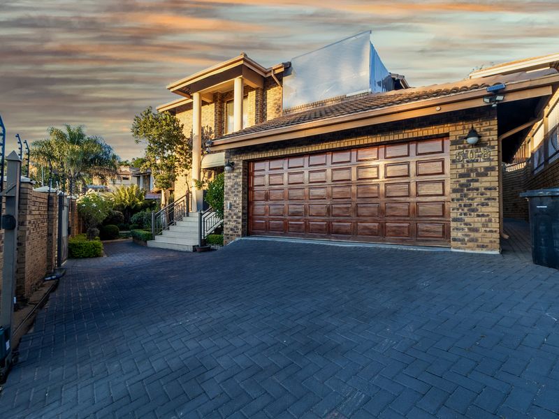 Front exterior view of a brick house featuring a paved driveway, double garage, and secure perimeter fencing.