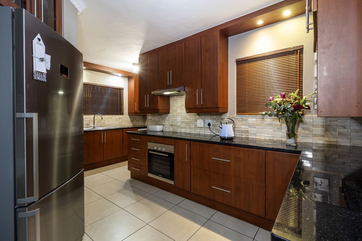 A well-maintained kitchen featuring dark wood cabinetry, granite countertops, stainless steel oven, extractor fan, and neutral tiled flooring.