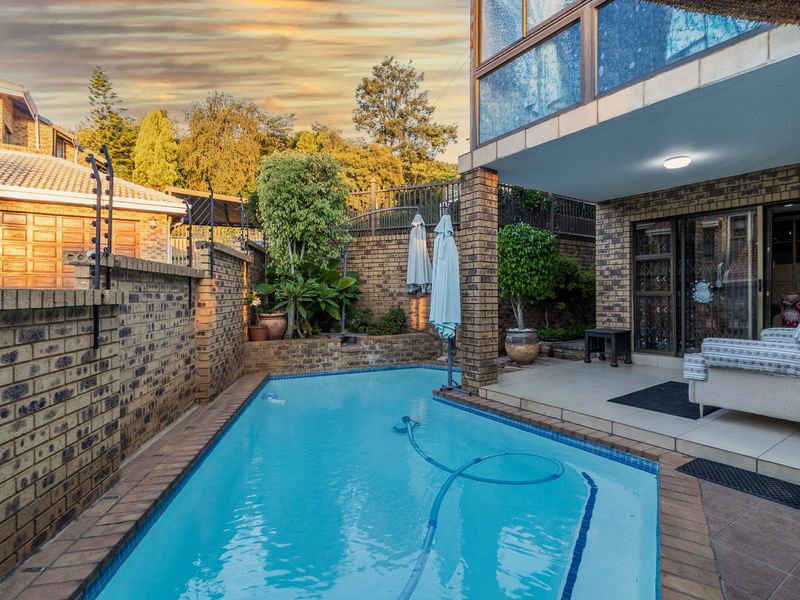 Outdoor pool area featuring a tiled patio, brick boundary walls with electric fencing, and direct access to the home via sliding glass doors.