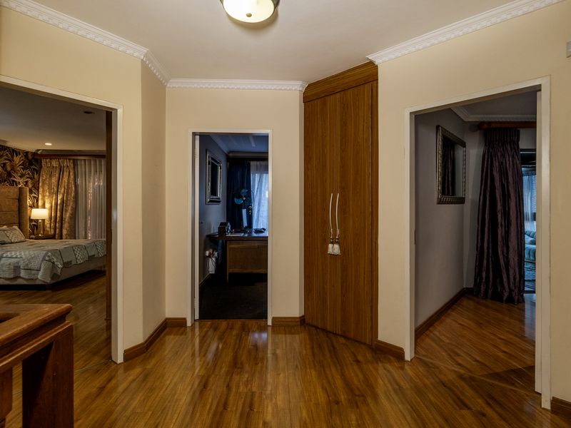 A well-maintained hallway featuring laminate flooring, crown molding, and a built-in wooden cupboard, providing access to multiple rooms.
