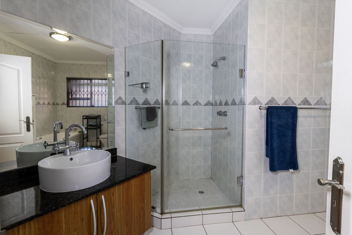 A well-maintained bathroom featuring a modern vessel sink on a granite vanity, a glass-enclosed shower, and neutral wall tiling.