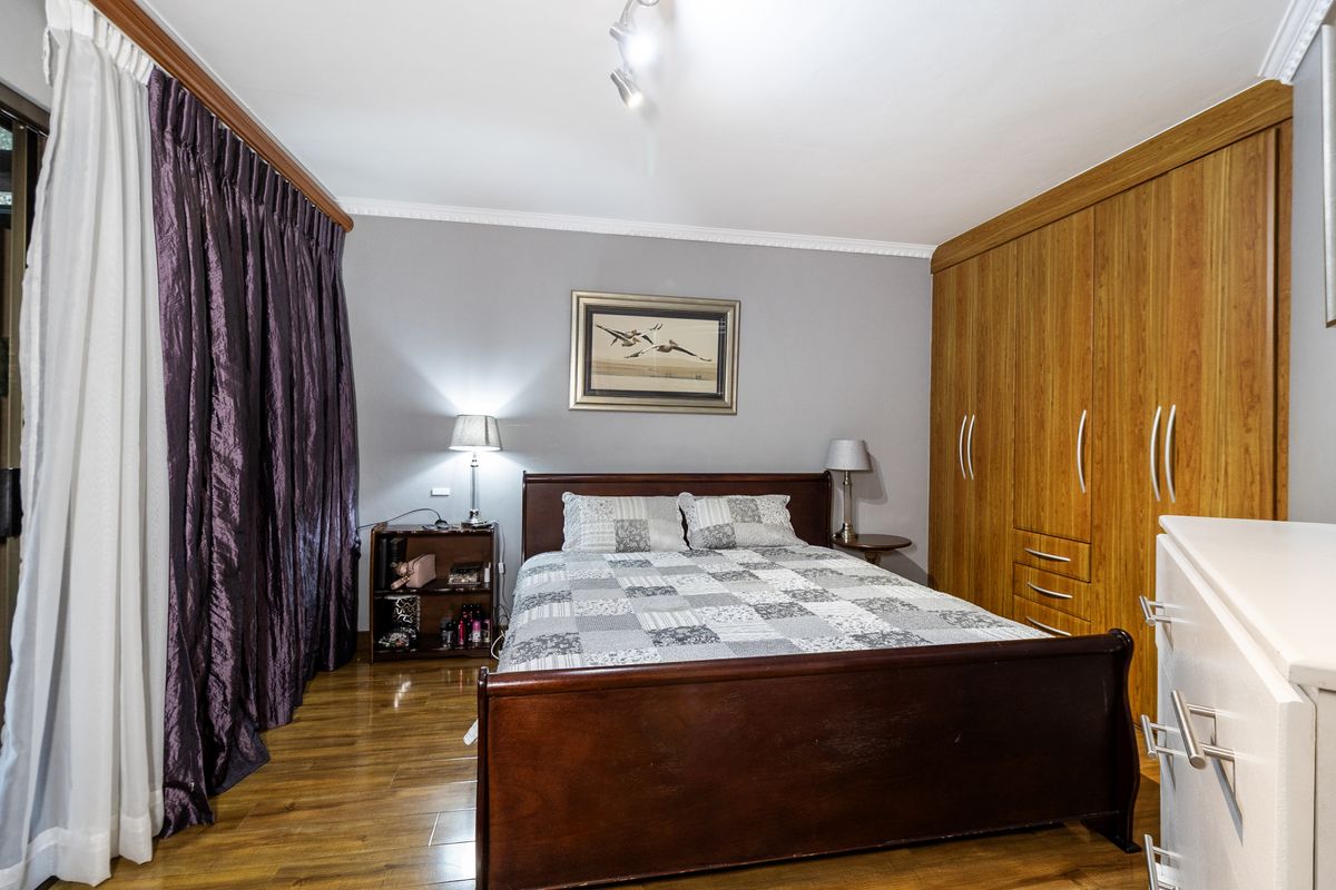 A well-maintained bedroom featuring laminate flooring, crown molding, and extensive built-in wooden wardrobe storage.