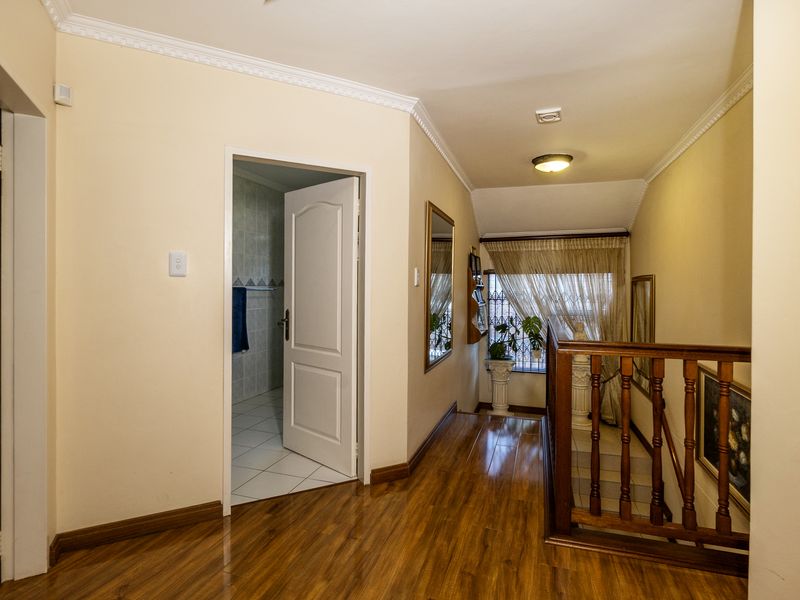 A well-lit hallway featuring laminate flooring, crown molding, and a wooden staircase railing, providing access to adjacent rooms.
