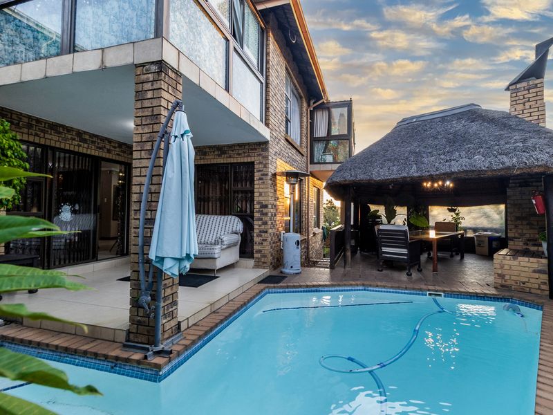 Outdoor entertainment area featuring a swimming pool, a covered patio, and a traditional thatched lapa, perfect for relaxed outdoor living.