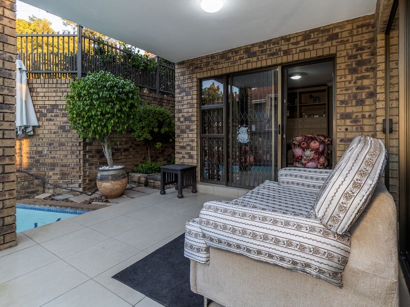 A covered patio area featuring tiled flooring, brick walls, and direct access to a swimming pool through sliding glass doors.