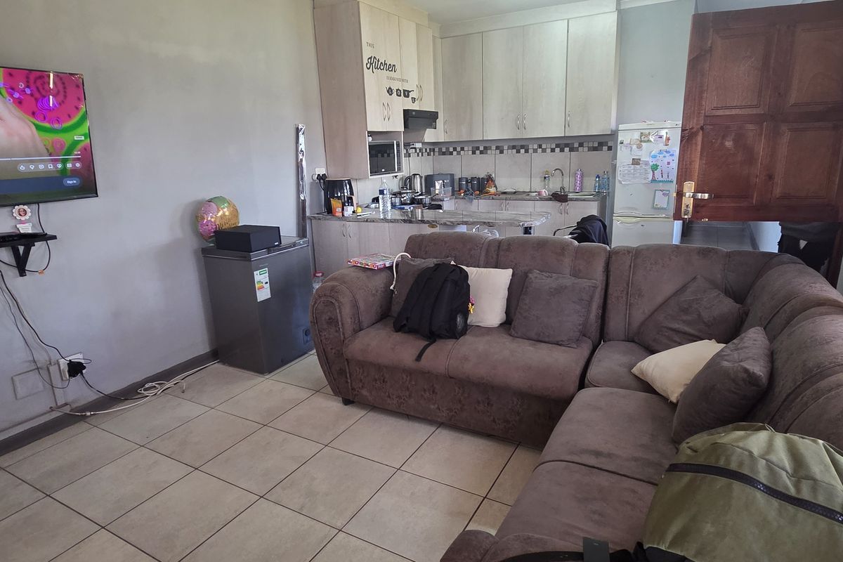 Open-plan living area featuring a compact kitchen with built-in cabinetry, tiled flooring, and a functional layout connecting the kitchen and lounge space.