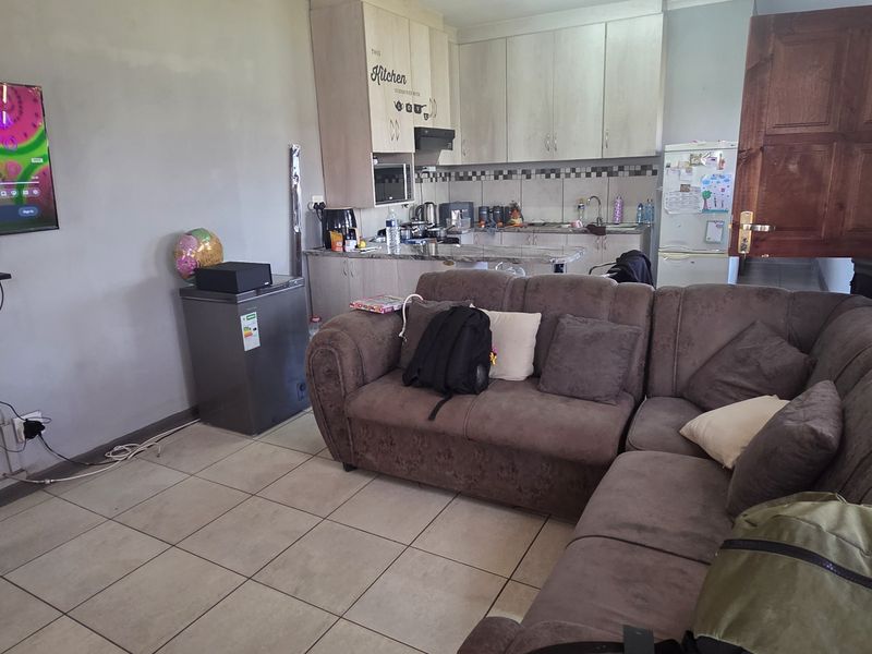 Open-plan living area featuring a compact kitchen with built-in cabinetry, tiled flooring, and a functional layout connecting the kitchen and lounge space.