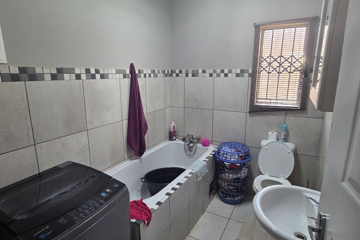 A functional bathroom featuring a built-in bathtub, pedestal basin, toilet, and neutral ceramic tiling throughout.