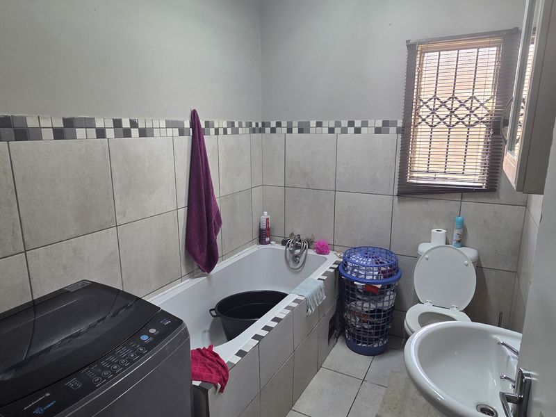 A functional bathroom featuring a built-in bathtub, pedestal basin, toilet, and neutral ceramic tiling throughout.