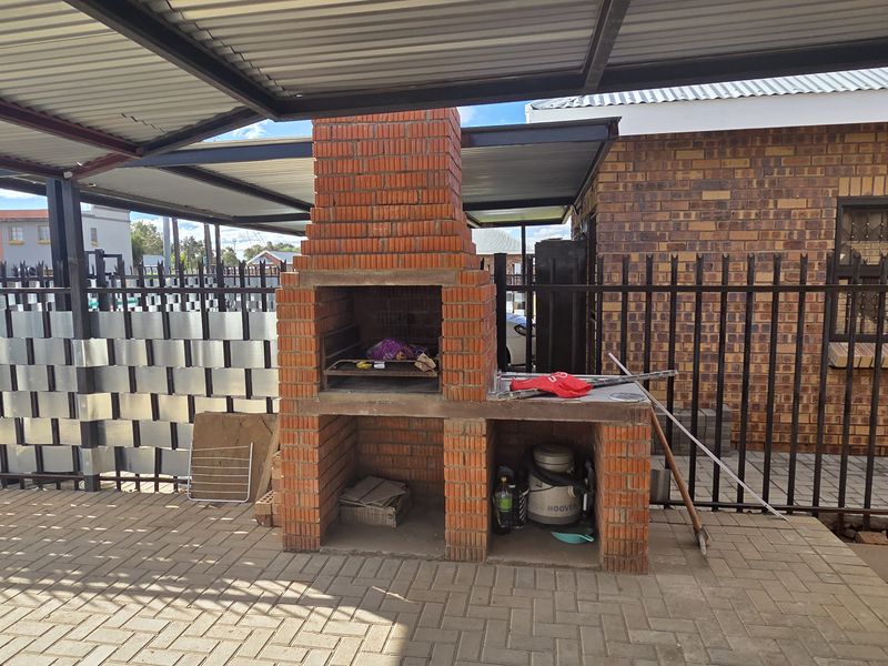 Covered outdoor patio area featuring a brick built-in braai, paved flooring, and secure metal fencing, ideal for outdoor entertaining.