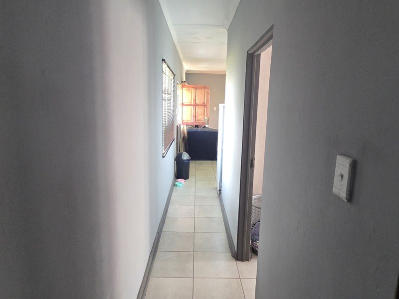 A functional hallway featuring neutral tiled flooring and natural light through a side window, providing access to adjacent rooms.