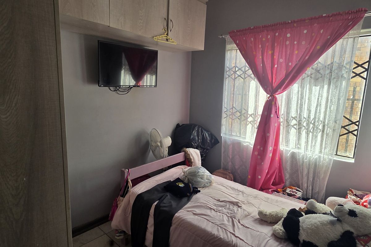 A functional bedroom featuring built-in cupboards with overhead storage, tiled flooring, and a window fitted with a security gate.