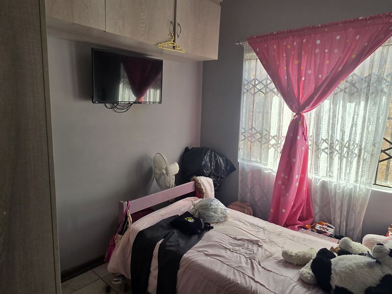 A functional bedroom featuring built-in cupboards with overhead storage, tiled flooring, and a window fitted with a security gate.