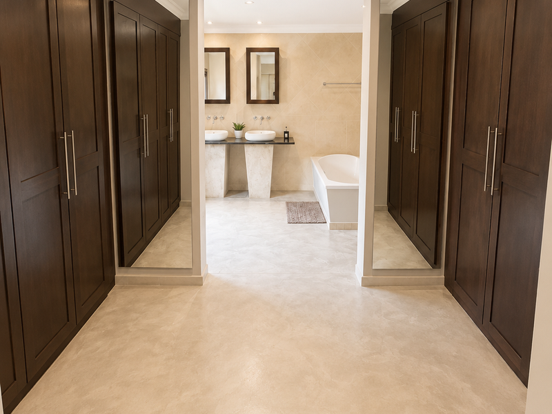 Spacious primary bathroom featuring extensive built-in dark wood cabinetry, a double vanity, and a sleek freestanding bathtub with neutral tiled finishes.