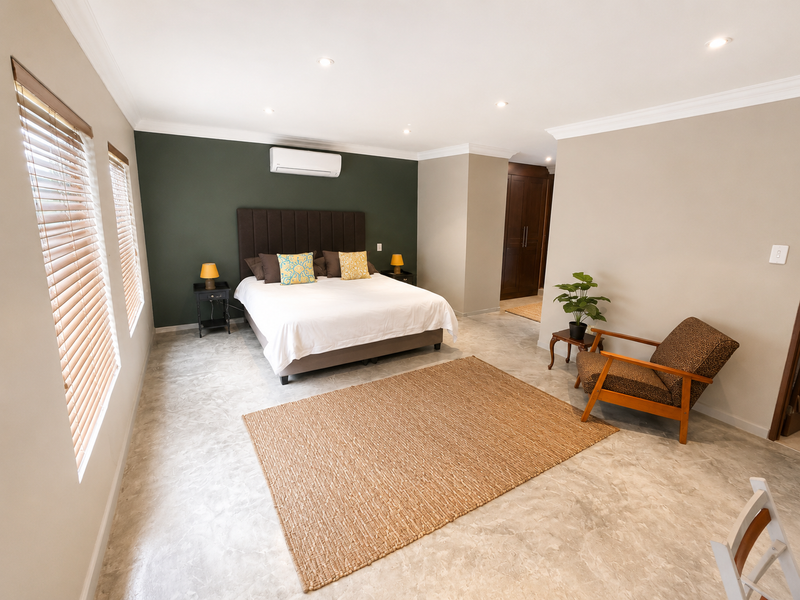 Spacious bedroom featuring polished concrete flooring, a dark green feature wall, built-in cupboards, and an integrated air conditioning unit.