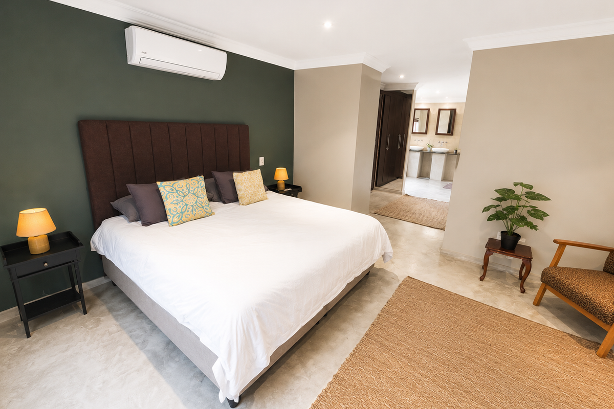 Spacious bedroom featuring polished concrete floors, a dark accent wall, air conditioning, and an open-plan en-suite bathroom with a double vanity.