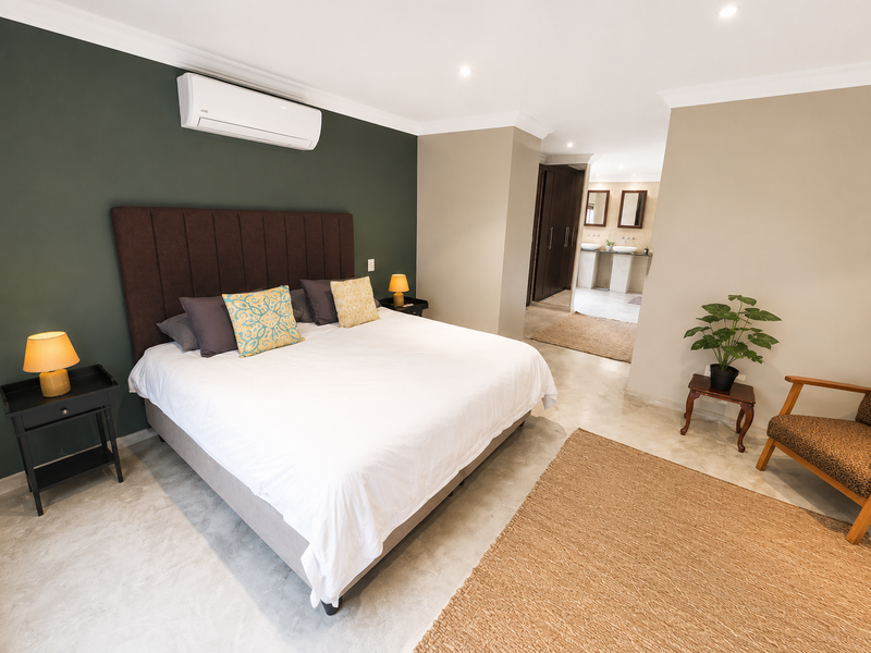 Spacious bedroom featuring polished concrete floors, a dark accent wall, air conditioning, and an open-plan en-suite bathroom with a double vanity.