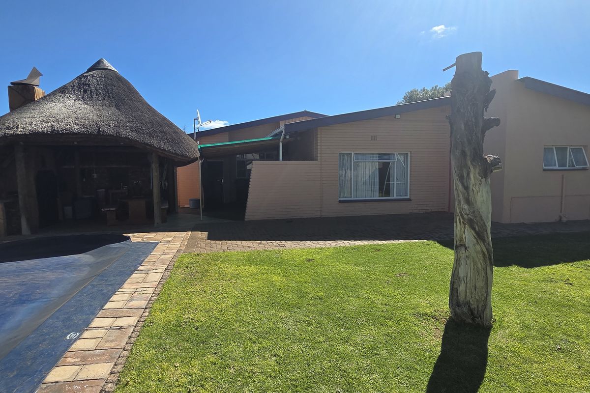 Rear garden area featuring a swimming pool, paved patio, and a traditional thatched lapa, providing an outdoor entertainment space.