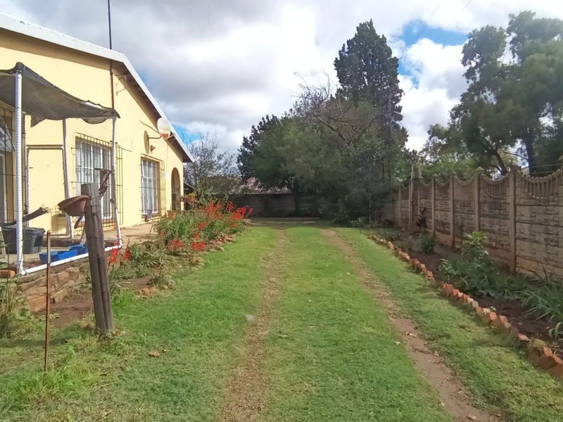 A view of the rear garden area featuring a lawn, established garden beds, and a precast concrete boundary wall along the property perimeter.